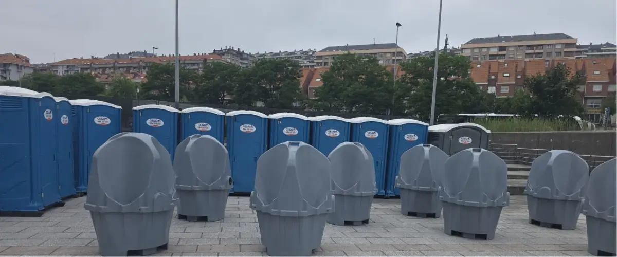 Batería de cabinas azules y urinarios portátiles de Gesal en un recinto exterior